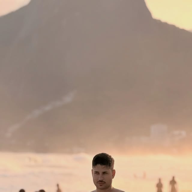 Pablo na praia com montanhas ao pôr do sol
